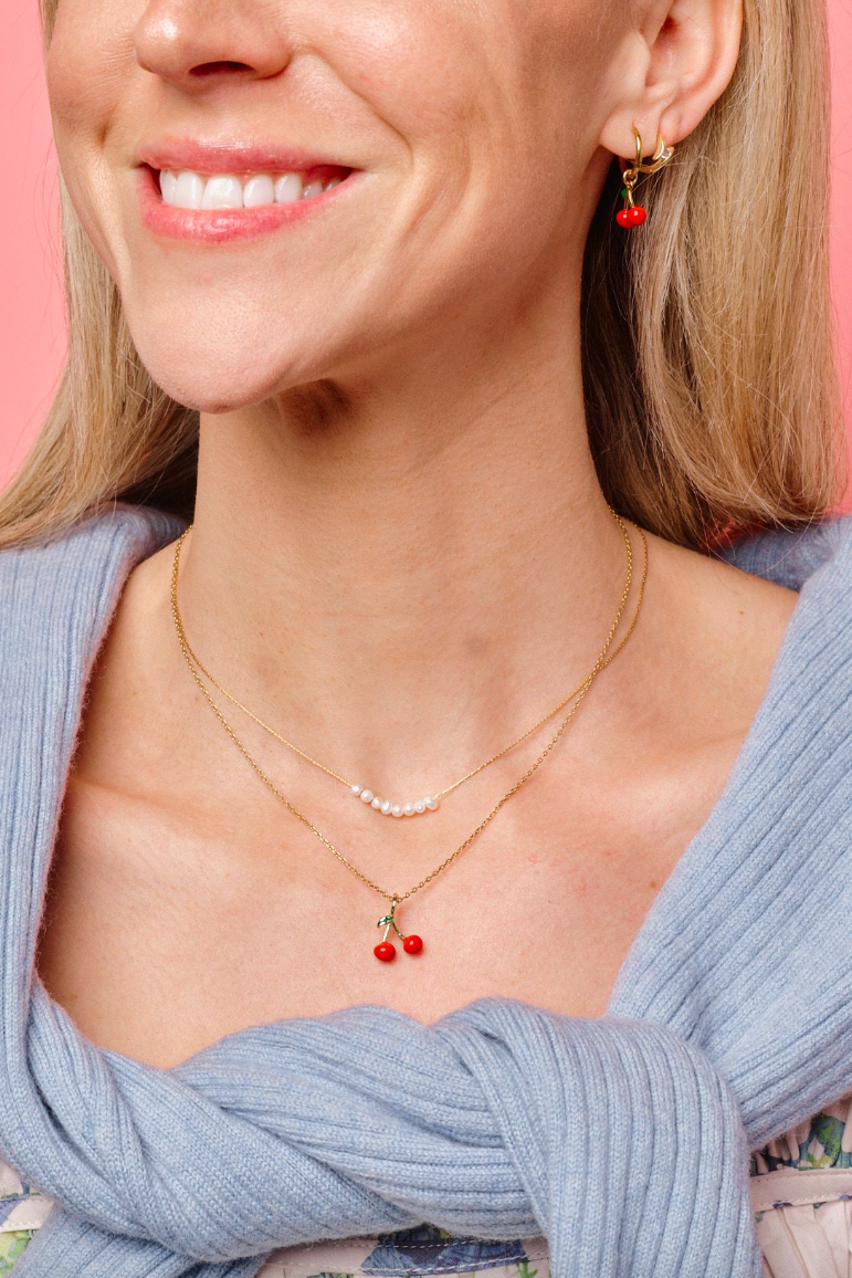 Woman wearing a gold necklace with red beads against a pink background