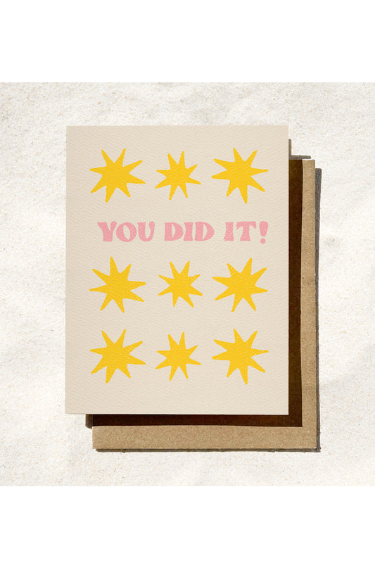 Greeting card with yellow stars and 'YOU DID IT!' text on a textured surface