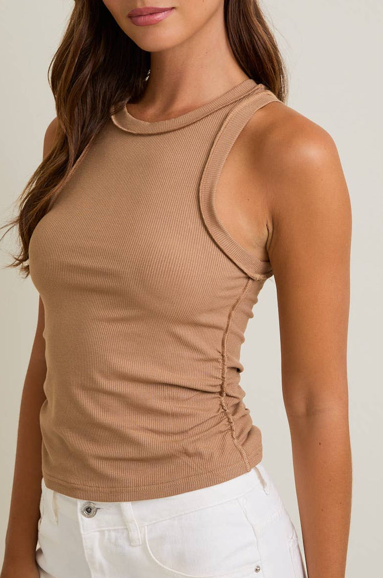 Woman wearing a beige sleeveless top against a plain background