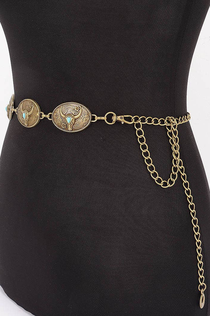 An antique bronze belt with three oval decorative medallions and turquoise accents, displayed on a black mannequin torso against a white background.