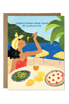 Greeting card with illustration of a woman at an outdoor table with food and drink, with text 'Cheers to many more years of La Dolce Vita'.
