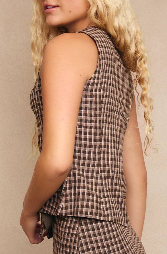 Person wearing a sleeveless checkered top and pants against a beige background