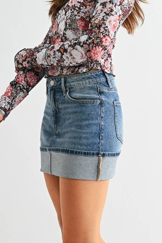 Woman wearing a floral blouse, denim skirt, and black knee-high boots on a white background