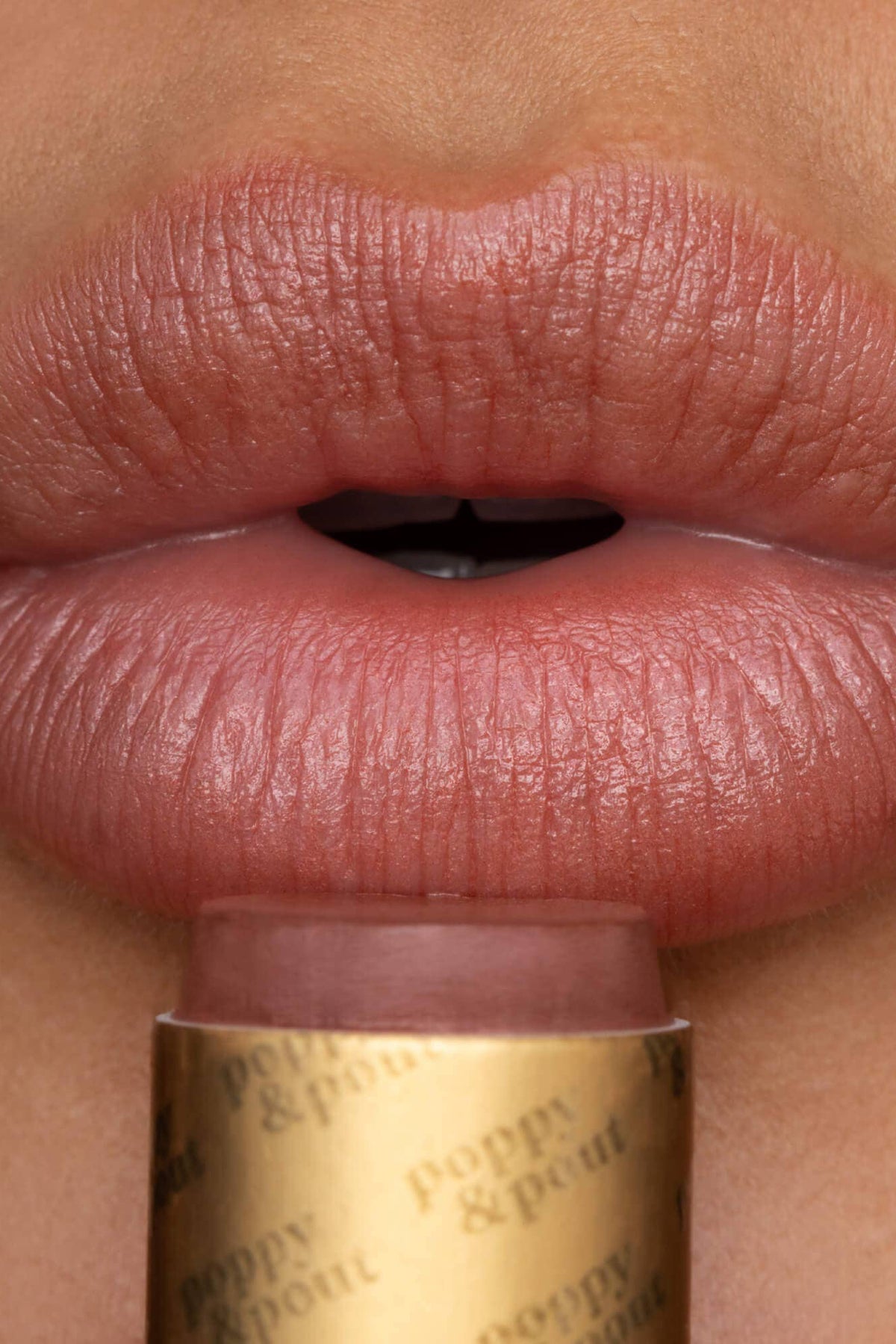 Close-up of a person applying pink lipstick to their lips with a gold tube labeled 'Poppy & Plum'.