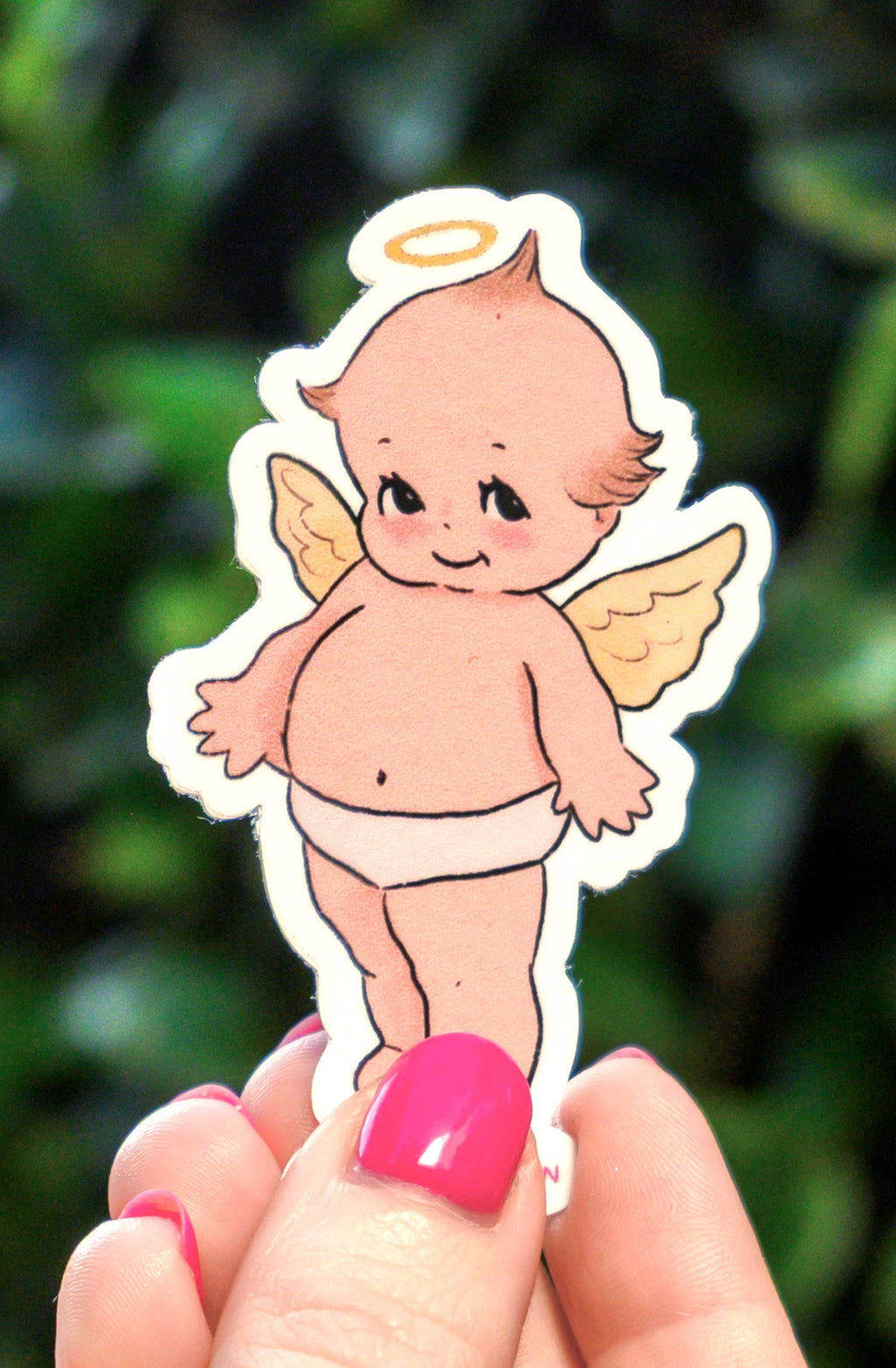 Hand holding a small angel sticker against a green leafy background