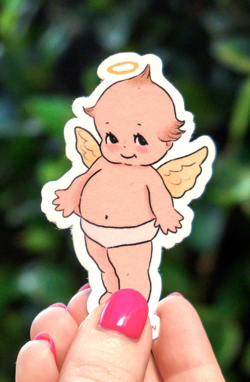 Hand holding a small angel sticker against a green leafy background
