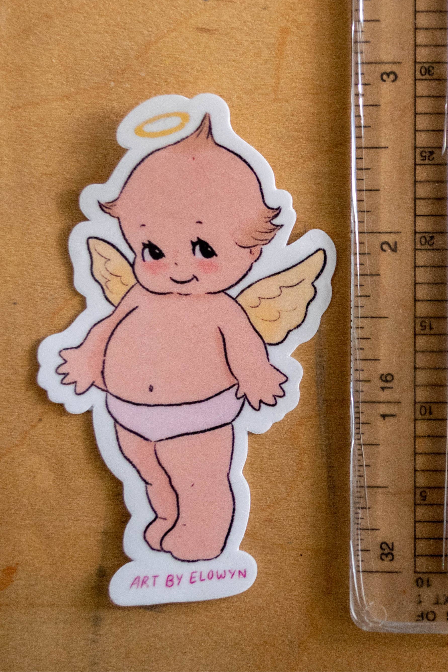 Sticker of an angelic figure next to a ruler on a wooden surface