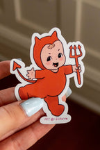 Hand holding a sticker of a small child in a devil costume against a neutral background