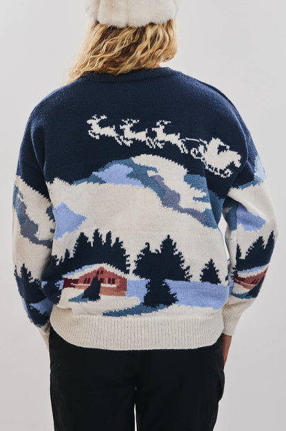 Person wearing a navy blue sweater with a winter scene design on a plain background
