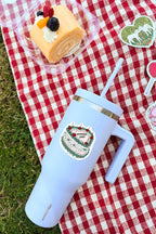 Light blue tumbler with a cake design on a red and white checkered tablecloth with a dessert in the background.