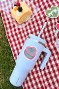 Light blue tumbler with a heart design on a red and white checkered tablecloth with a cake and decorative elements.