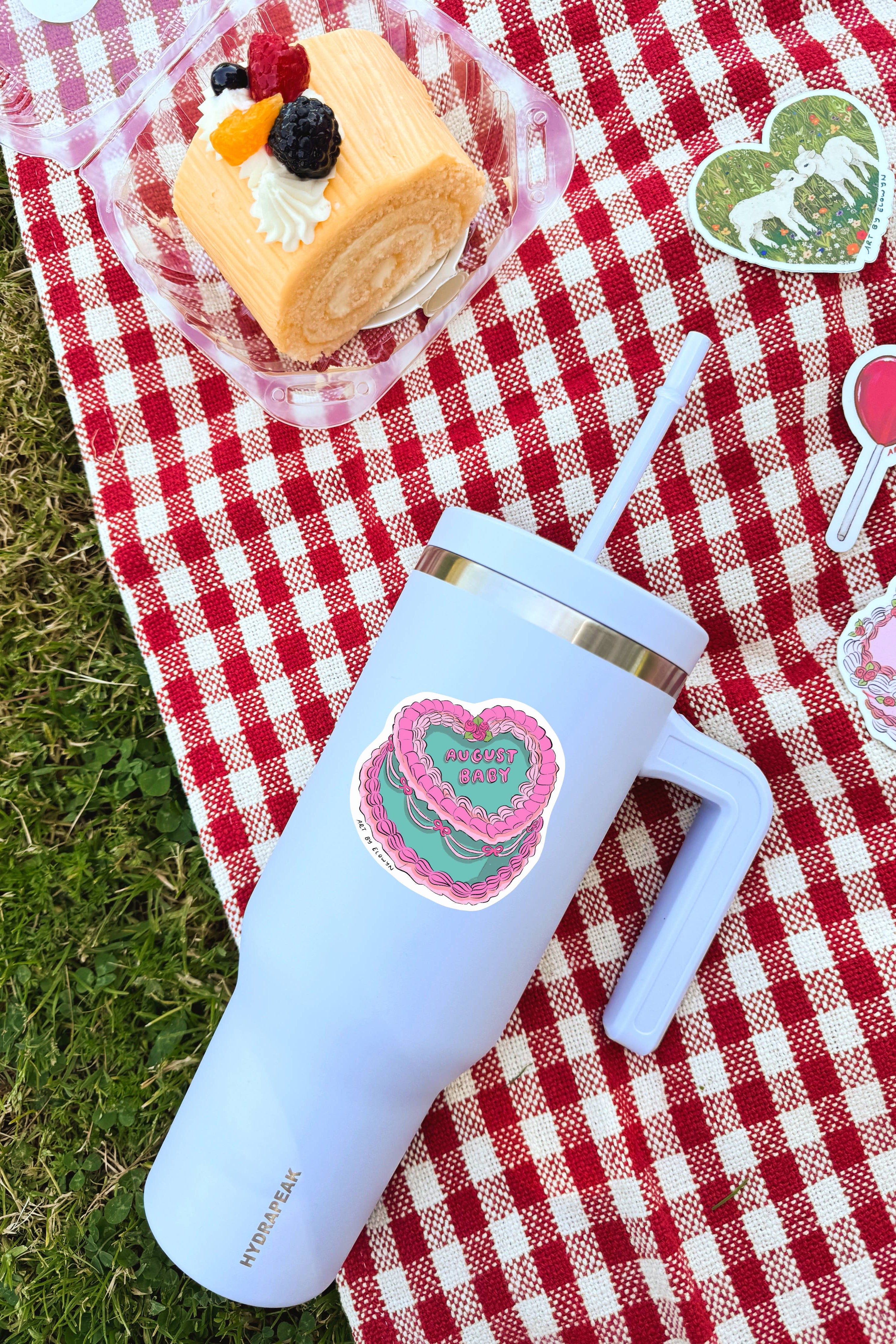 Light blue tumbler with a heart design on a red and white checkered tablecloth with a cake and decorative elements.