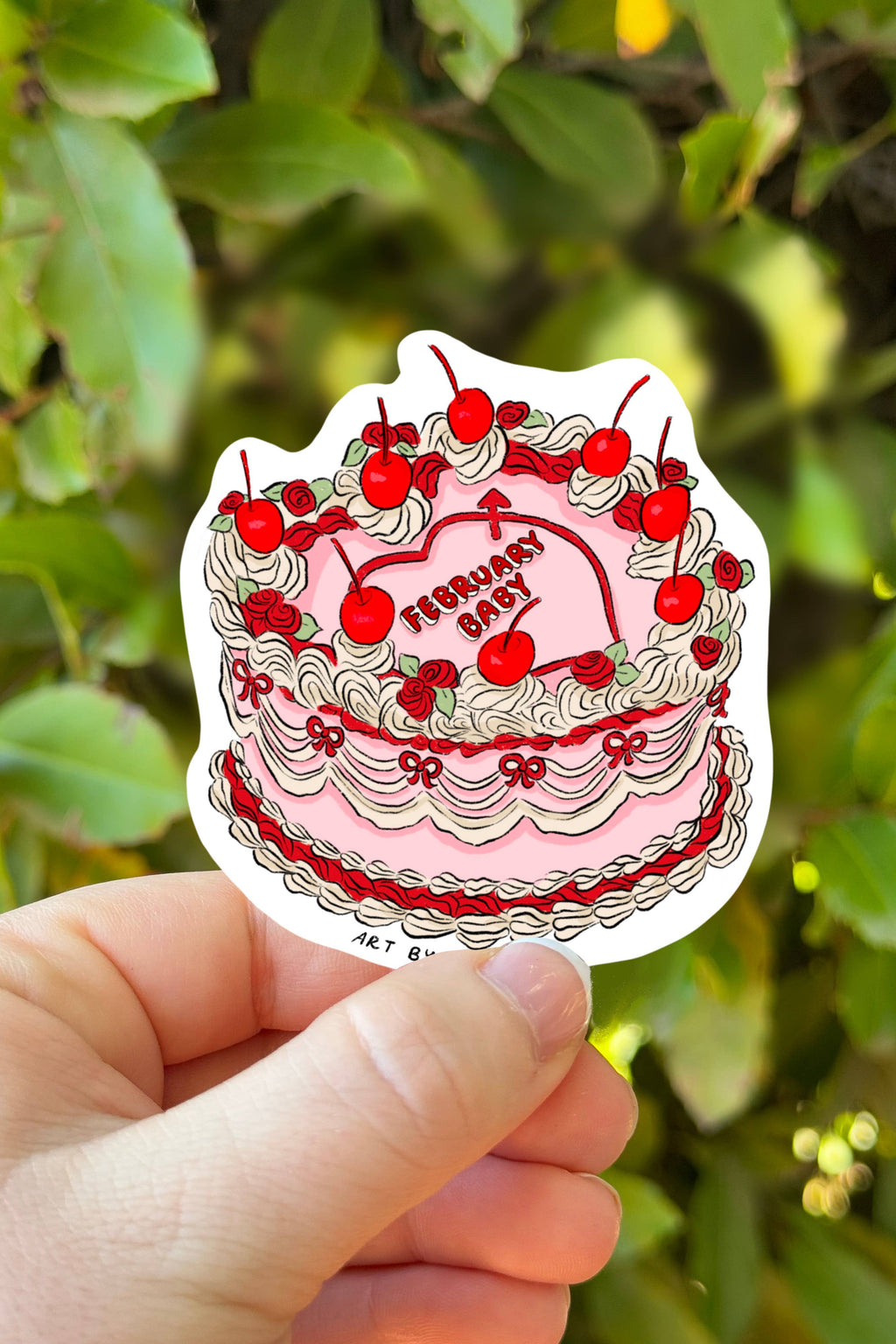 Sticker of a birthday cake with red cherries held in front of green foliage