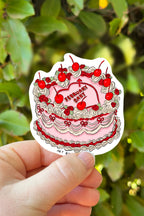 Sticker of a birthday cake with red cherries held in front of green foliage