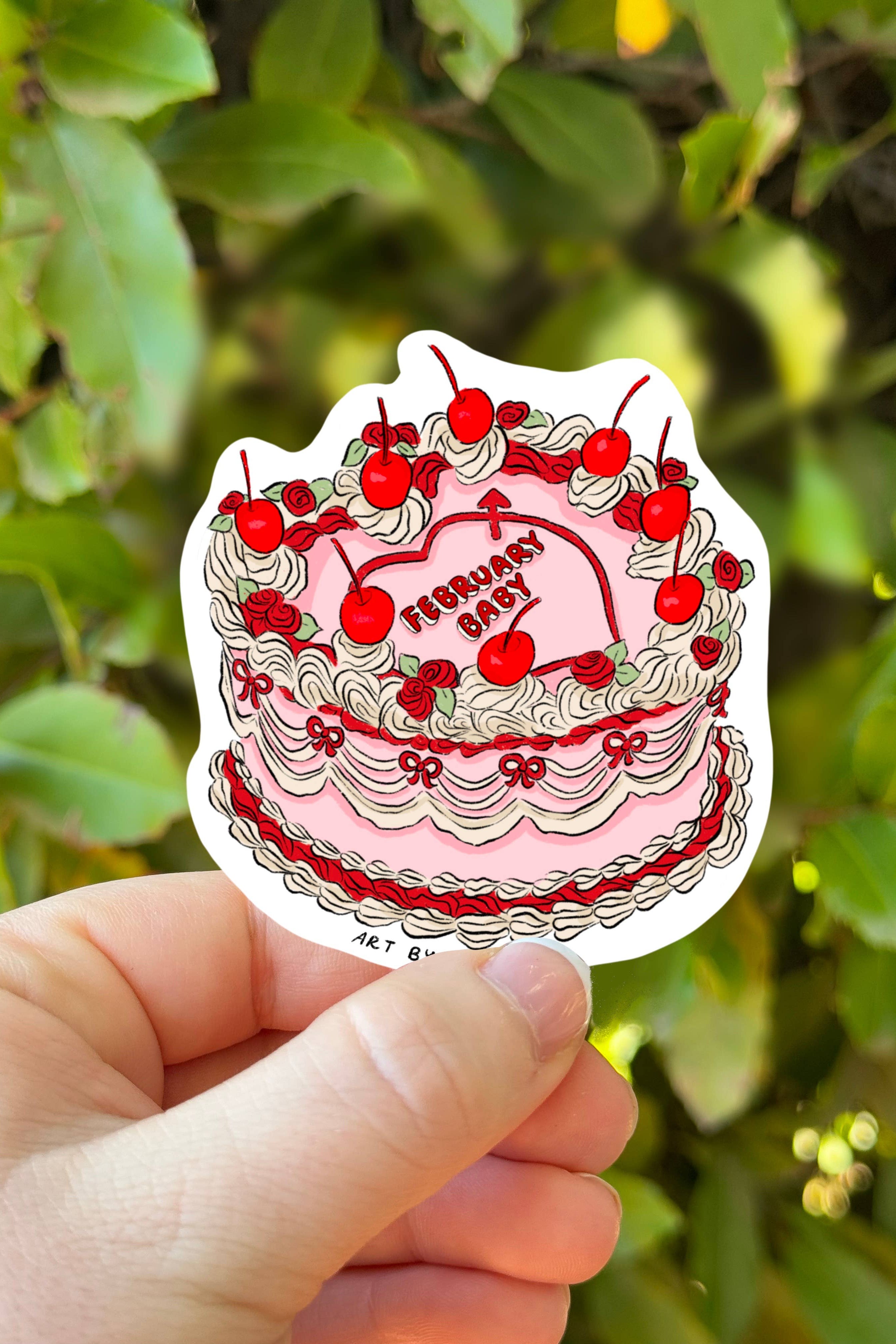 Sticker of a birthday cake with red cherries held in front of green foliage