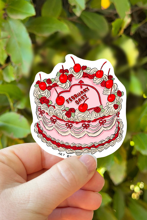 Sticker of a birthday cake with red cherries held in front of green foliage