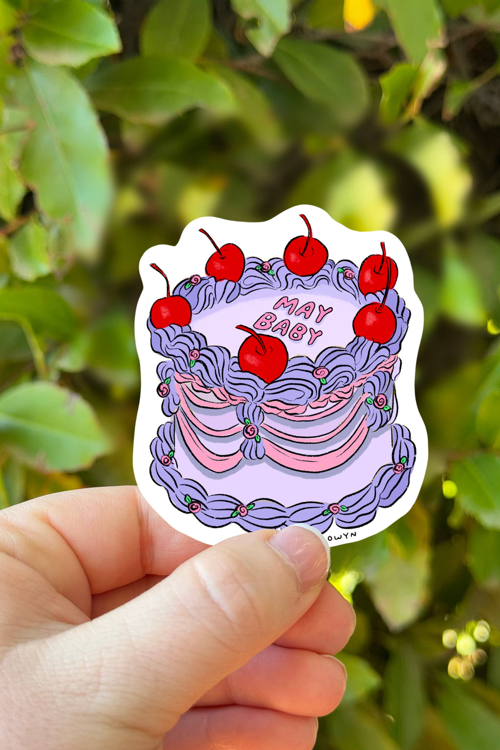 Sticker with cherries and text held by a hand against a green leafy background