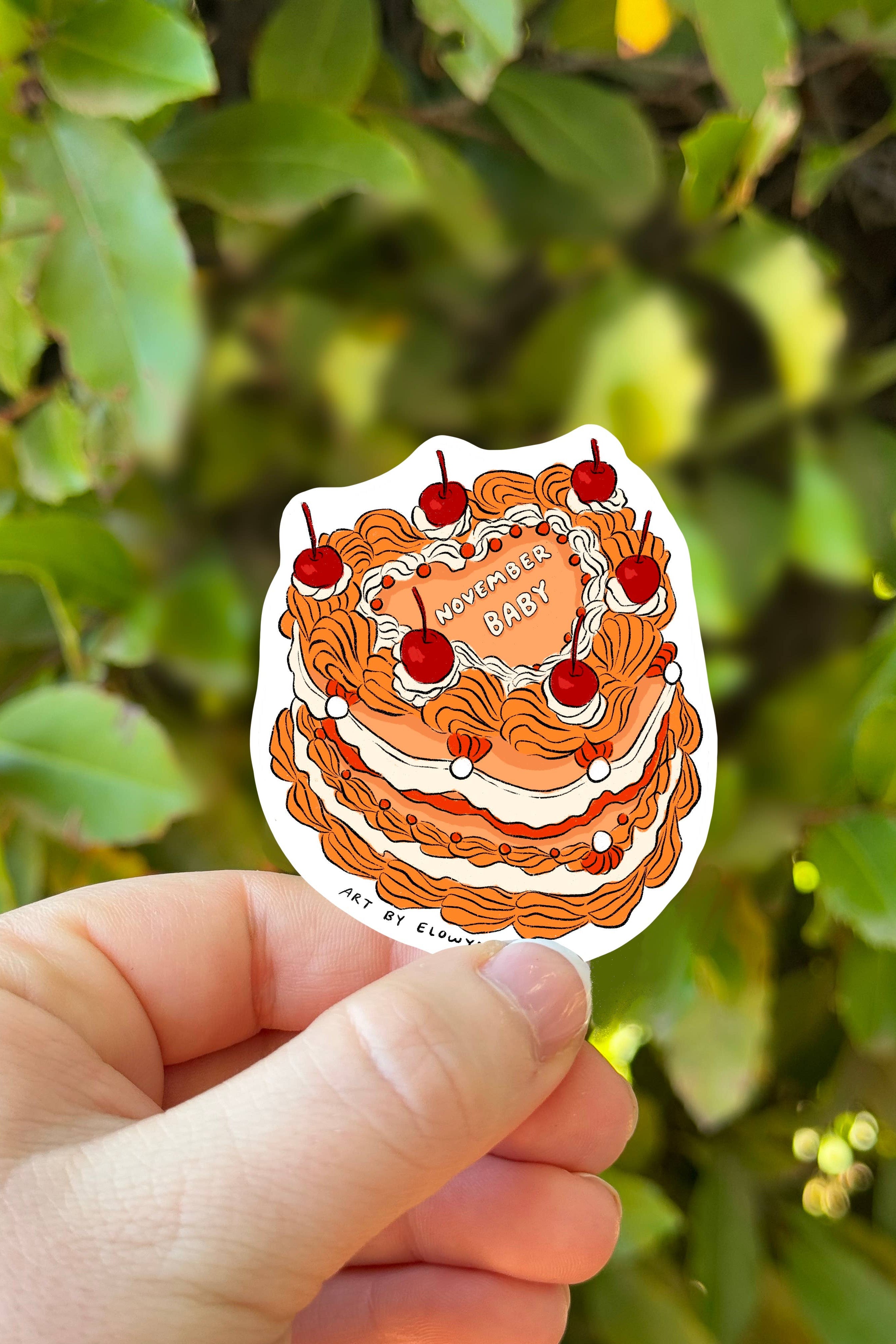 Sticker of a cake with cherries held in front of green foliage