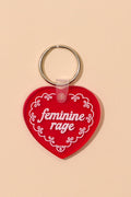 Red heart-shaped keychain with 'feminine rage' text on a beige background