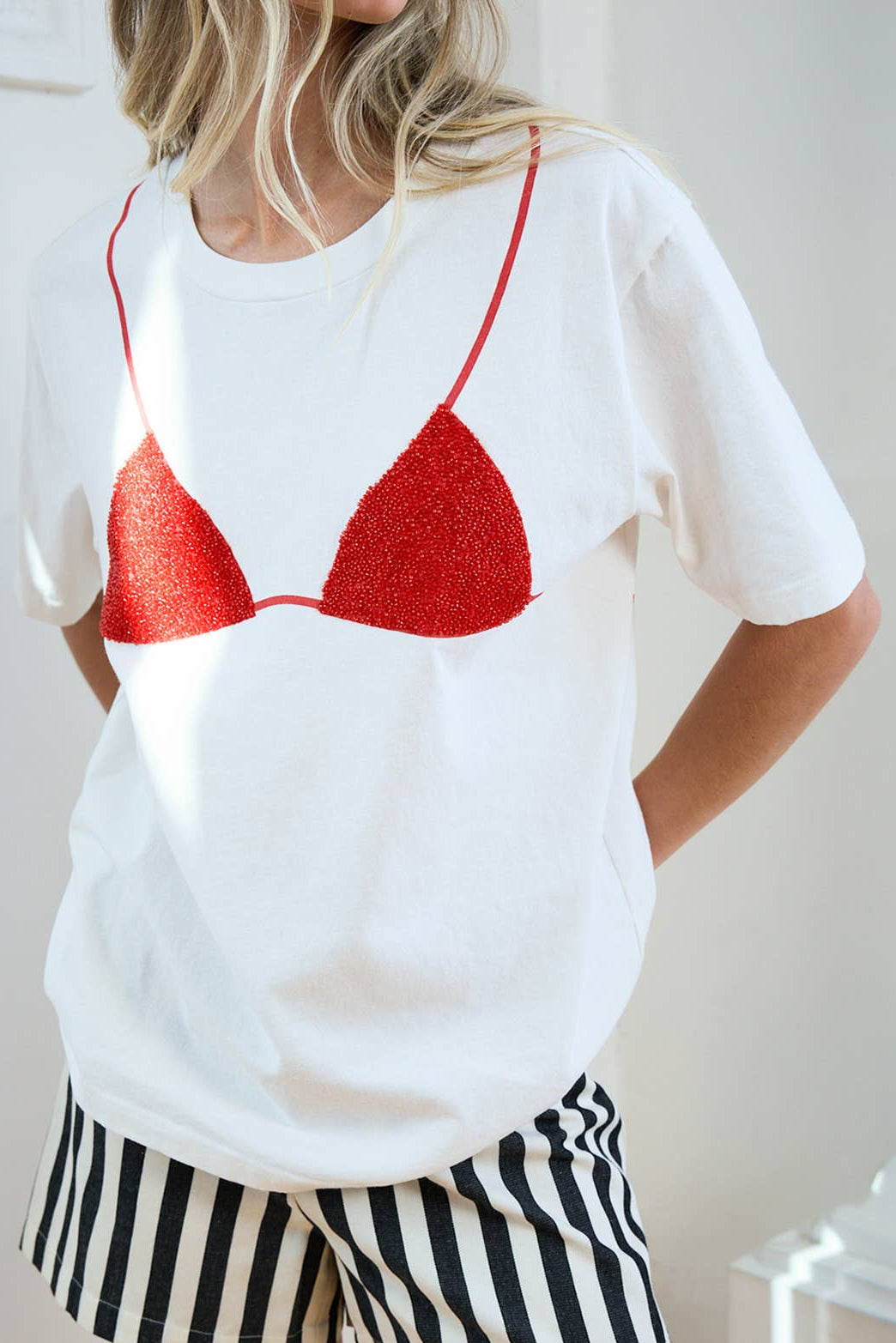 Person wearing a white t-shirt with a red bikini design and black and white striped shorts.