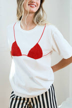 Woman wearing a white t-shirt with a red bra design and black and white striped shorts indoors.