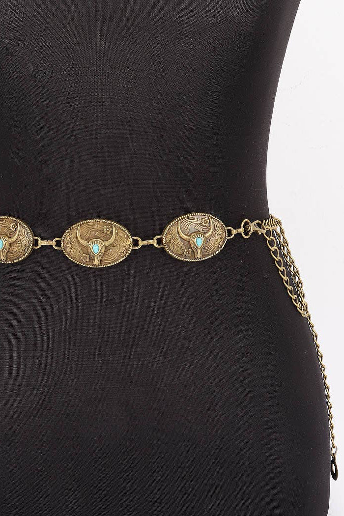 An antique bronze chain belt with three oval medallion charms featuring a stylized bull and turquoise accents, displayed on a black mannequin torso.