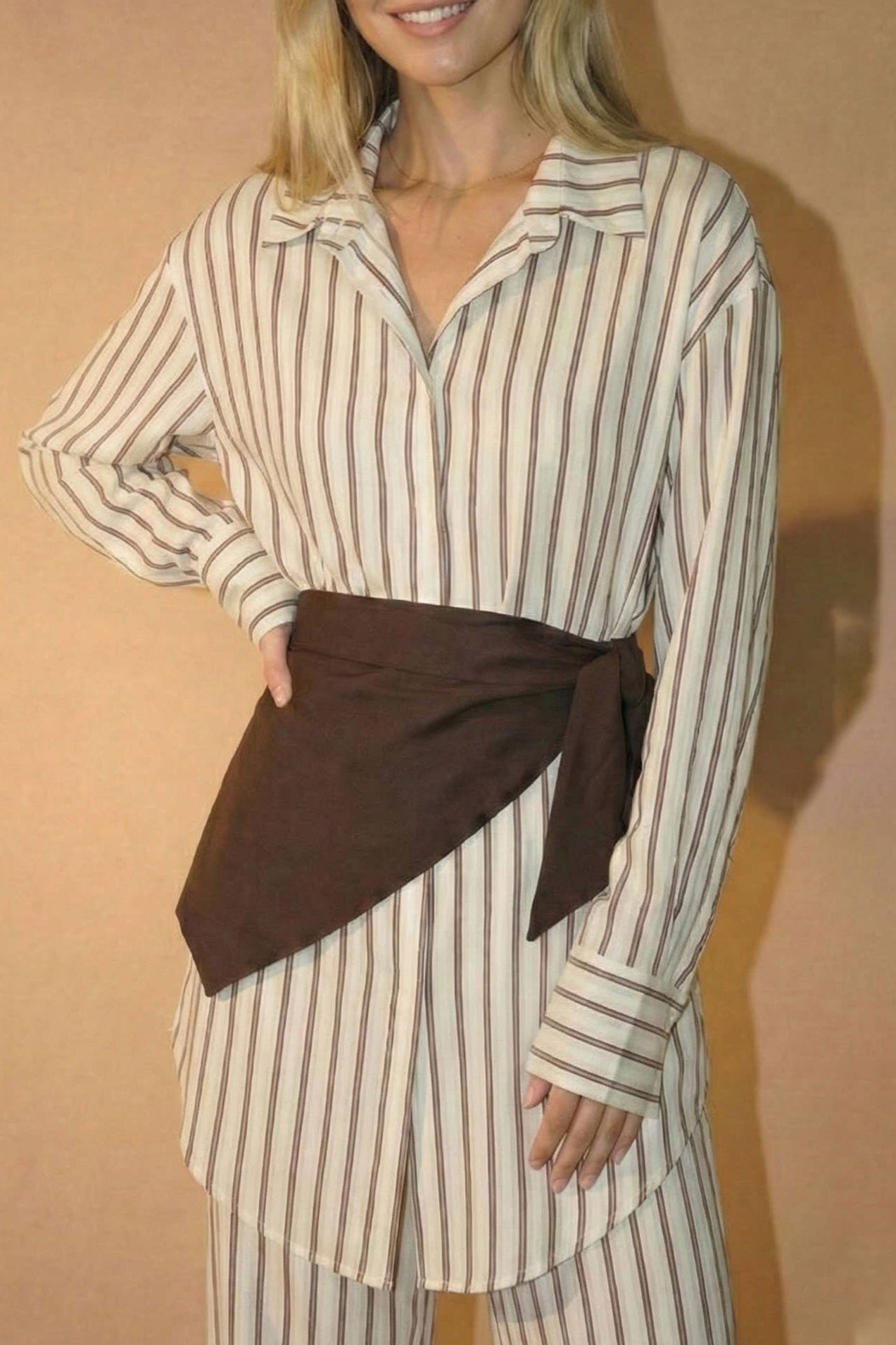 Woman wearing a striped outfit with a brown belt against a beige background