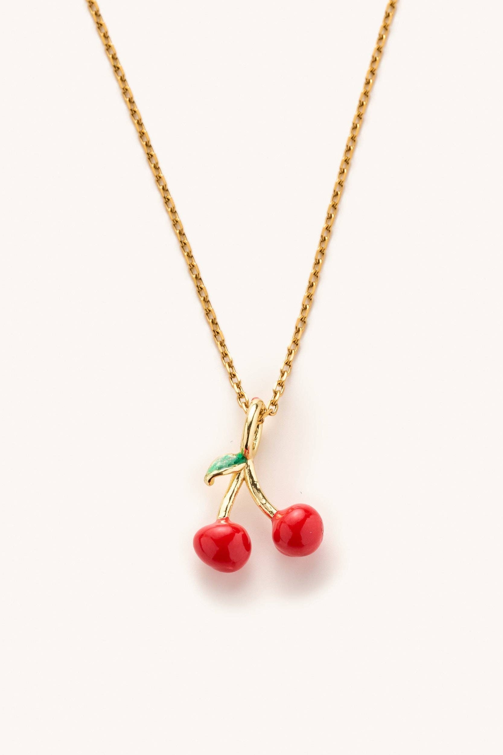 Gold necklace with cherry pendant on a white background