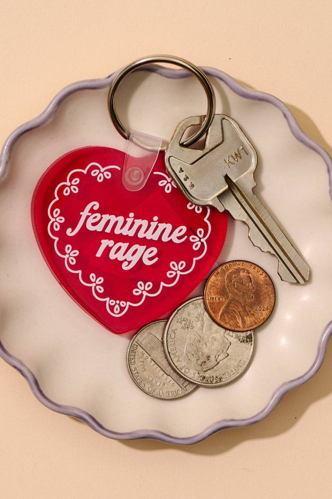 Keychain with 'feminine rage' on a heart-shaped tag on a beige background