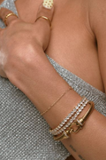 Close-up of a hand wearing gold rings and bracelets on a textured surface