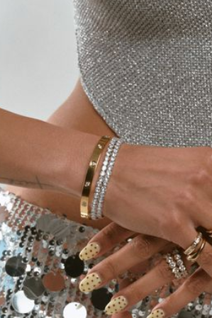 Close-up of hands wearing multiple rings and bracelets with a sequined outfit background