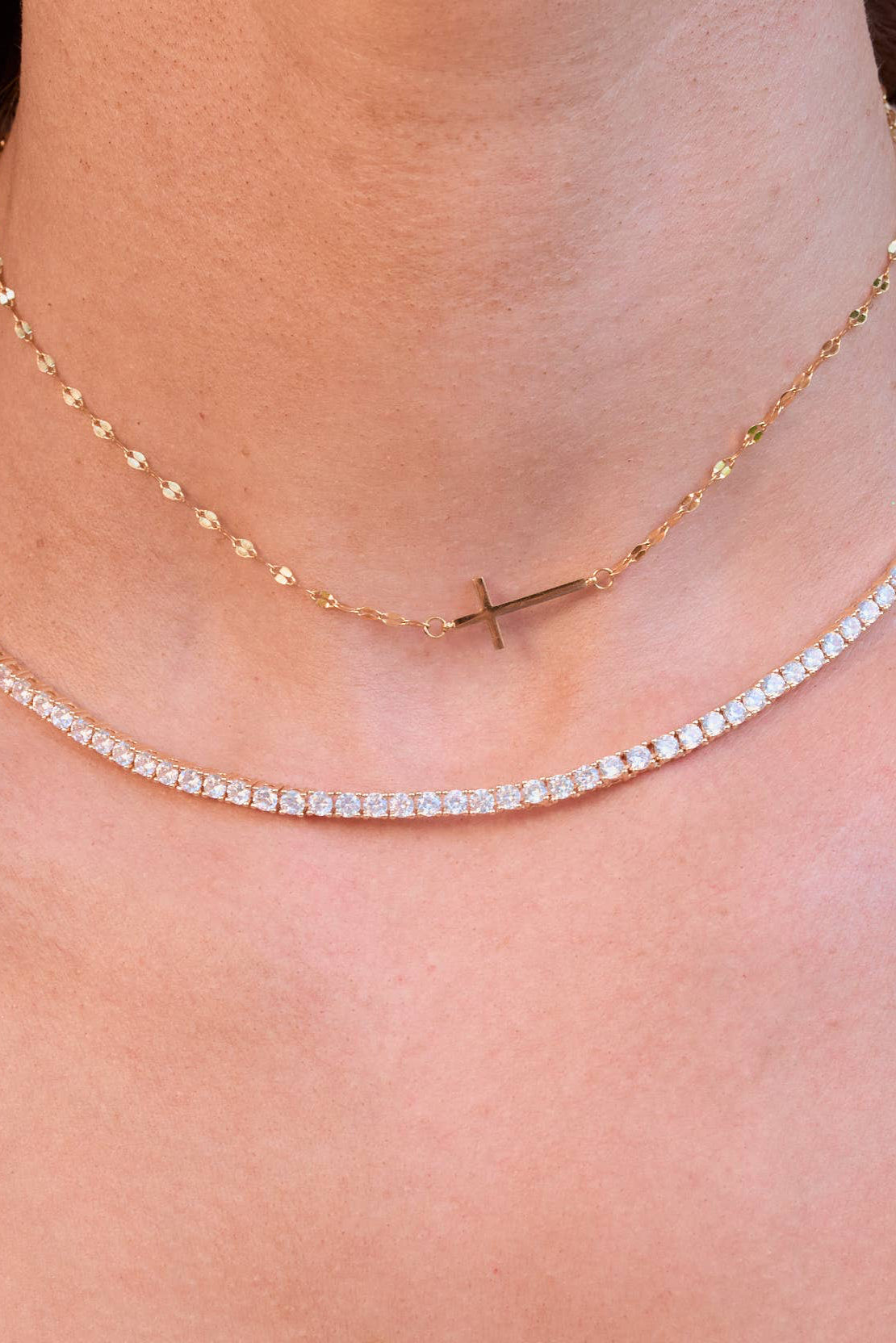 Close-up of a person wearing a delicate necklace with a cross pendant.