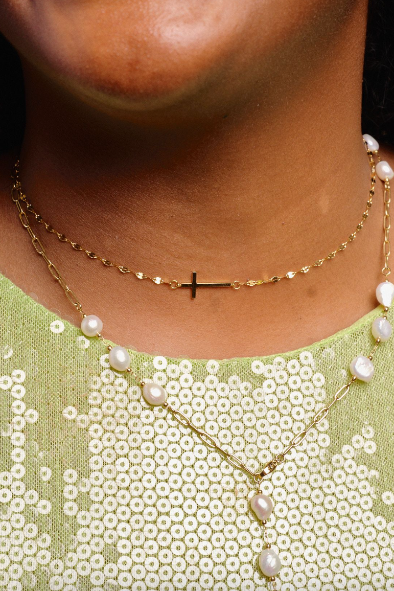 Close-up of a person wearing a gold necklace with pearl accents and a green sequined top.
