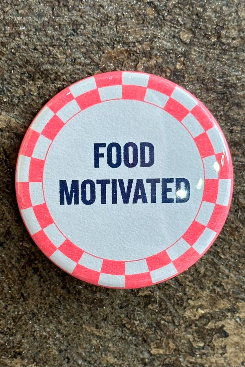 Button badge with 'FOOD MOTIVATED' text on a checkered border against a stone background