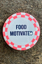 Button badge with 'FOOD MOTIVATED' text on a checkered border against a stone background
