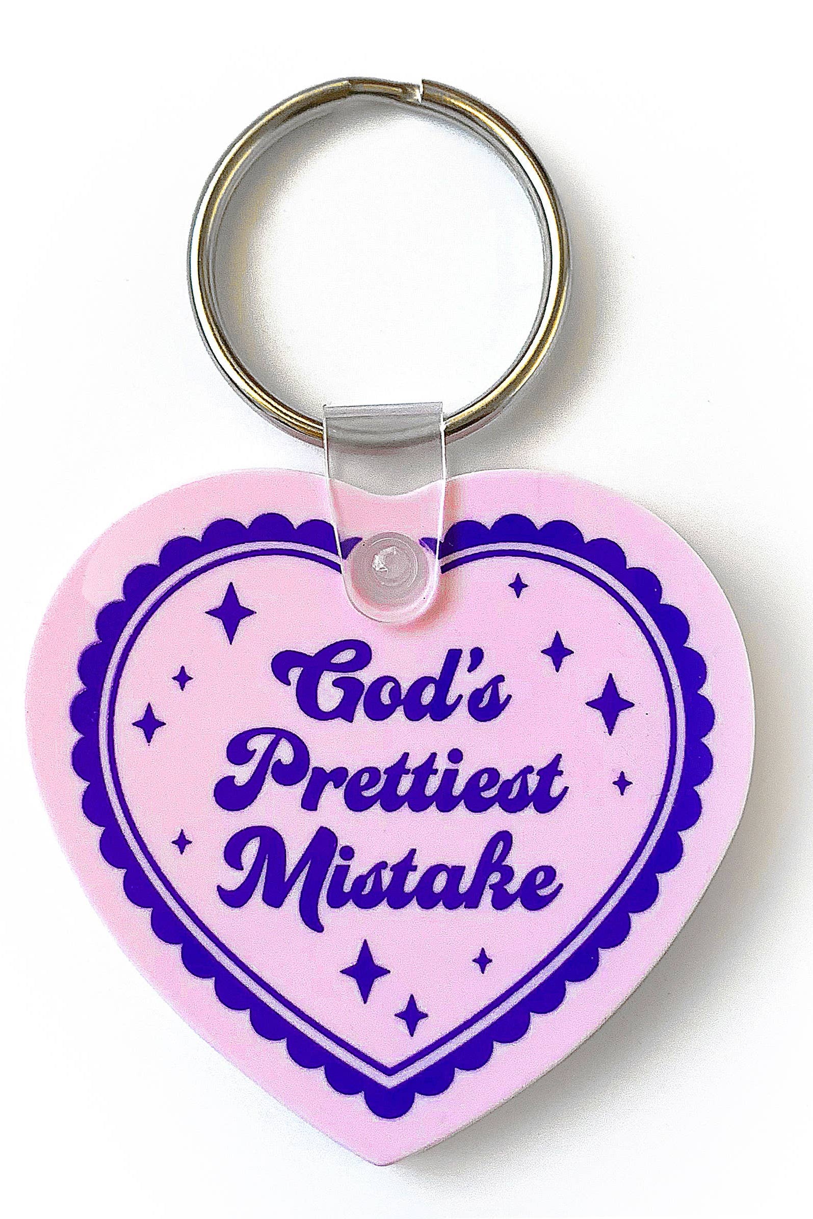 Heart-shaped keychain with 'God's Prettiest Mistake' text on a pink background