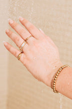 Hand with gold rings and bracelet against a beige background