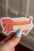 Hand holding a cartoon-style hot dog with mustard on a neutral background
