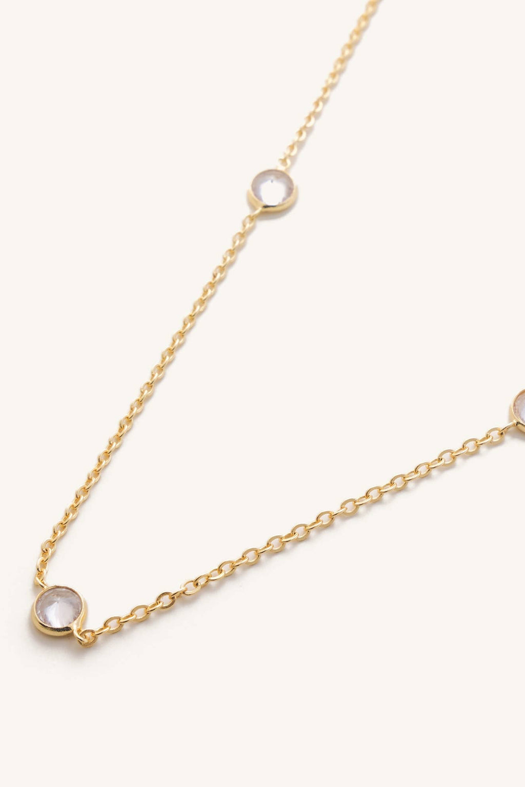 Gold necklace with small round diamonds on a light beige background