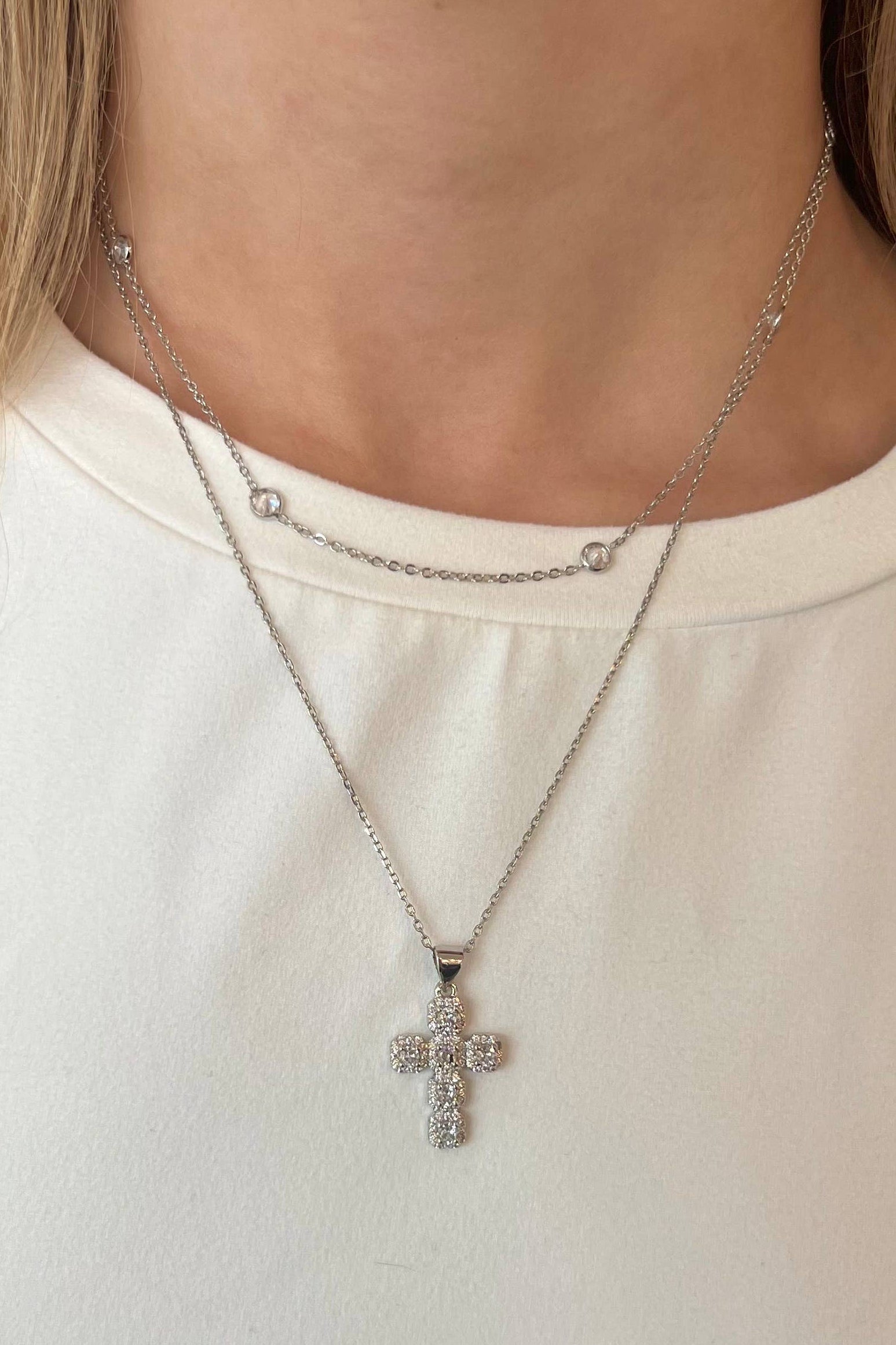 Silver necklace with a cross pendant worn by a person against a neutral background
