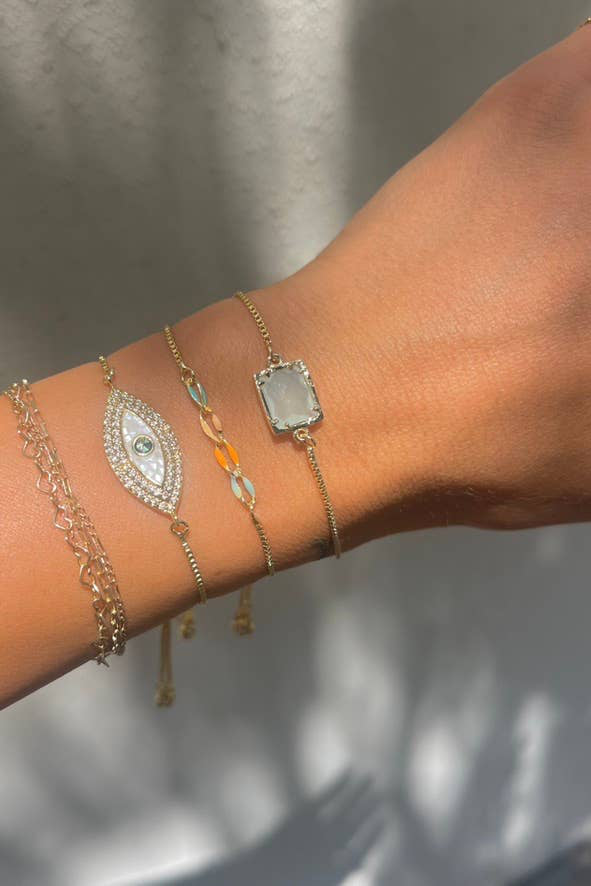 Close-up of a wrist wearing multiple gold bracelets with various designs on a neutral background