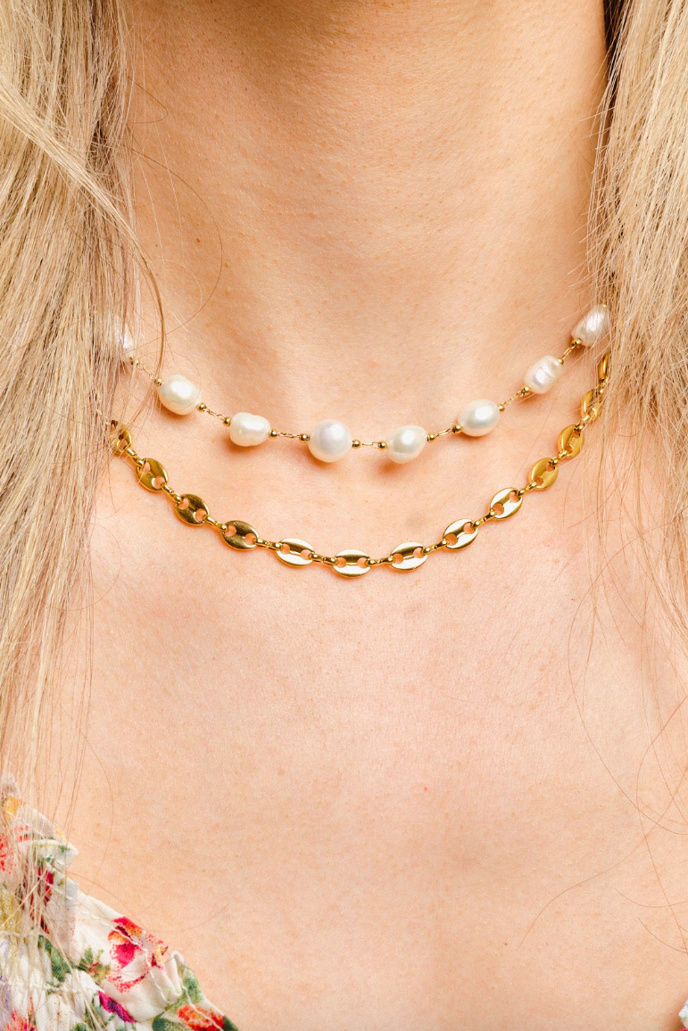 Two necklaces, one with pearls and the other gold chain, on a person with blonde hair.