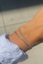 Close-up of a wrist wearing two gold bracelets with a blurred background