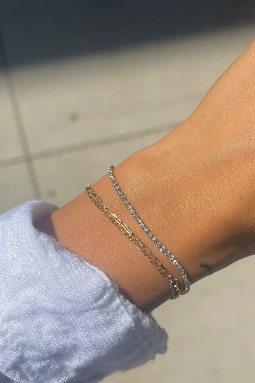 Close-up of a wrist wearing two gold bracelets with a blurred background