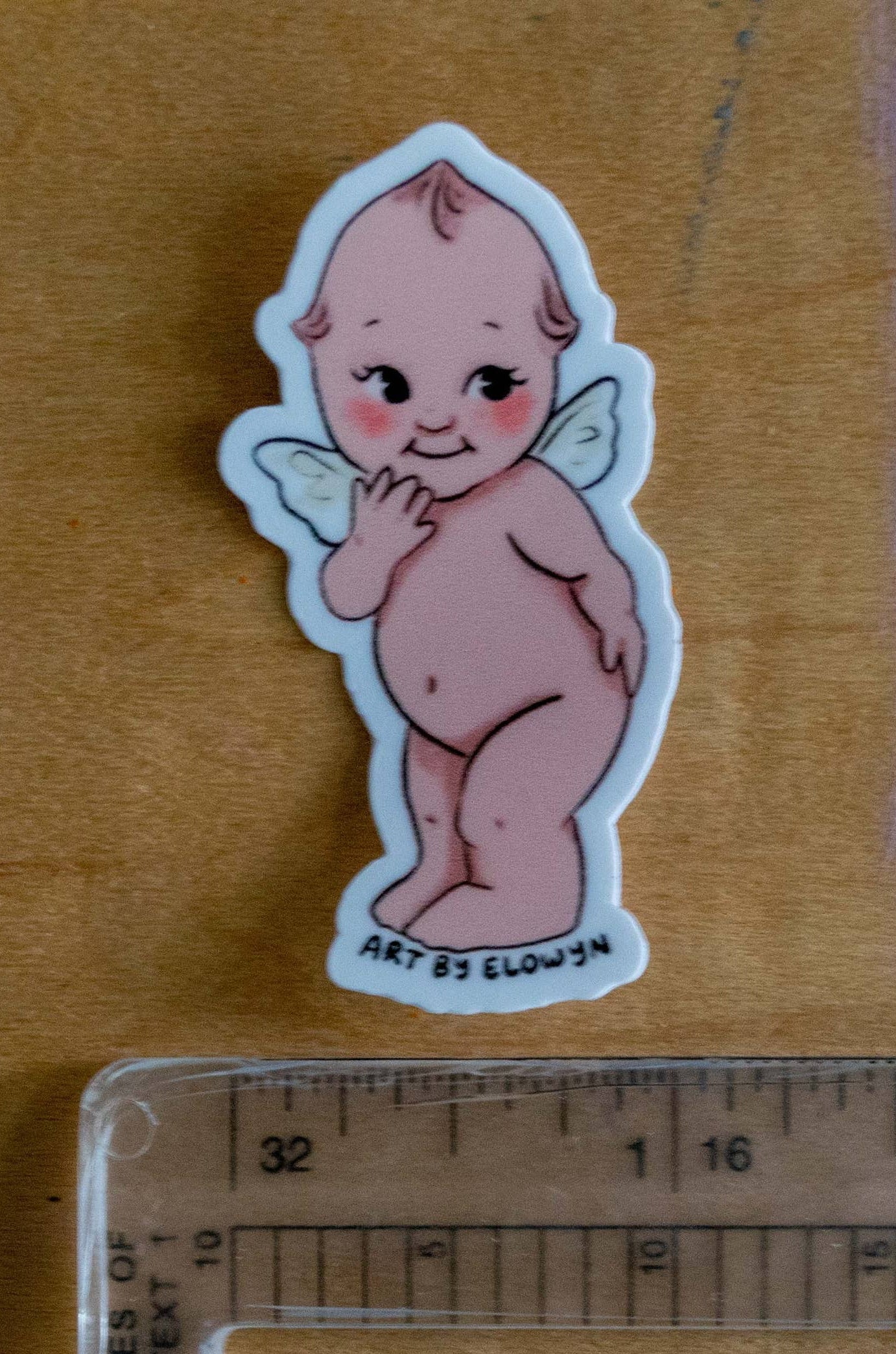 Small sticker of a cherubic figure next to a ruler on a textured surface