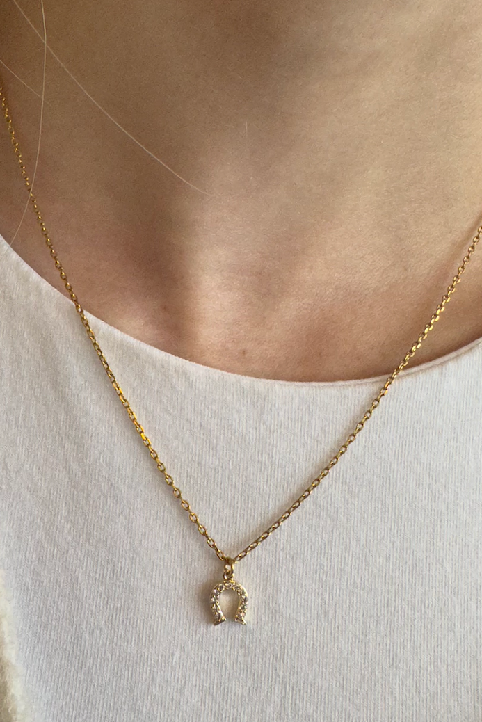 Gold necklace with a pendant worn by a person against a neutral background